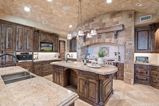 kitchen featuring tasteful backsplash, a center island with sink, sink, and decorative light fixtures