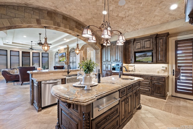 kitchen with hanging light fixtures, tasteful backsplash, sink, and a kitchen island with sink