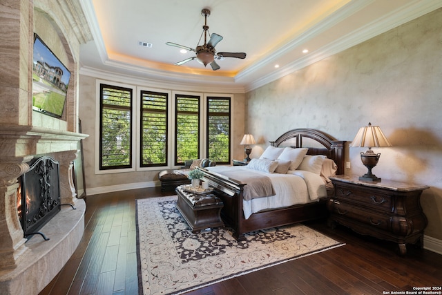 bedroom with ceiling fan, a premium fireplace, a raised ceiling, dark wood-type flooring, and crown molding