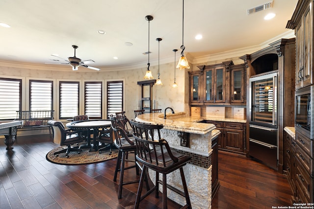 kitchen with kitchen peninsula, decorative light fixtures, ceiling fan, dark wood-type flooring, and ornamental molding