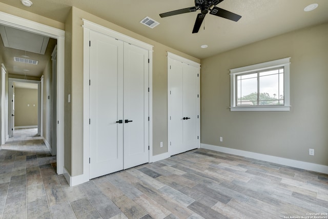 unfurnished bedroom with light hardwood / wood-style flooring, ceiling fan, and multiple closets