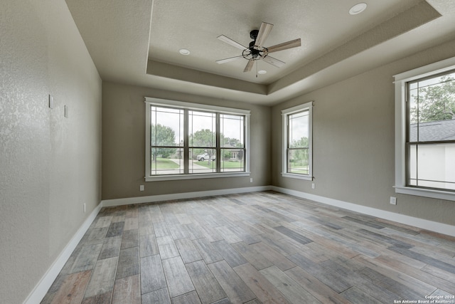 unfurnished room featuring light hardwood / wood-style floors, ceiling fan, a textured ceiling, and a tray ceiling