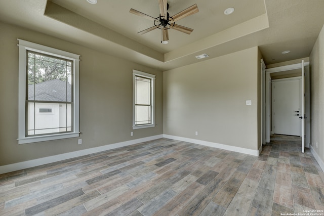 empty room with a raised ceiling, ceiling fan, and light wood-type flooring