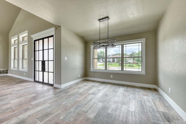 unfurnished dining area with an inviting chandelier, a textured ceiling, vaulted ceiling, and light wood-type flooring