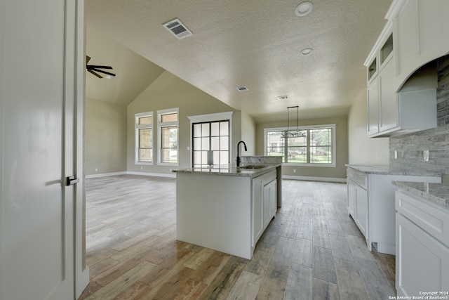 kitchen featuring white cabinets, tasteful backsplash, light wood-type flooring, and a kitchen island with sink