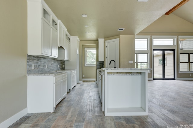 kitchen with light stone countertops, backsplash, hardwood / wood-style flooring, a kitchen island with sink, and white cabinets