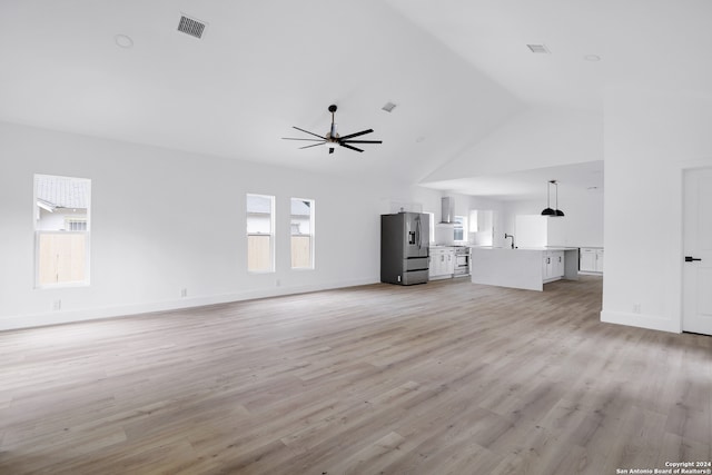 unfurnished living room featuring high vaulted ceiling, ceiling fan, a healthy amount of sunlight, and light wood-type flooring