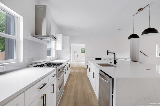 kitchen with appliances with stainless steel finishes, sink, wall chimney range hood, decorative light fixtures, and light hardwood / wood-style flooring