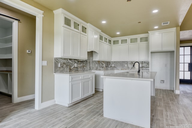 kitchen with white cabinets, tasteful backsplash, and a kitchen island with sink