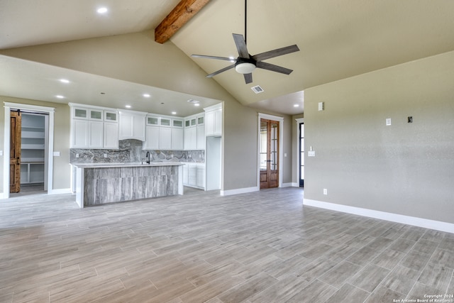 unfurnished living room with high vaulted ceiling, beam ceiling, sink, light hardwood / wood-style floors, and ceiling fan