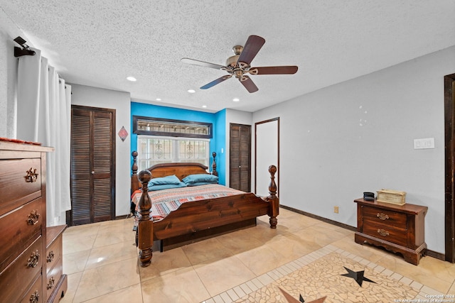 bedroom featuring ceiling fan, light tile patterned floors, and multiple closets