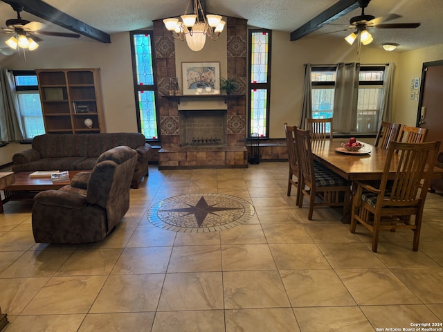 tiled dining room featuring a textured ceiling, a stone fireplace, ceiling fan with notable chandelier, and vaulted ceiling with beams