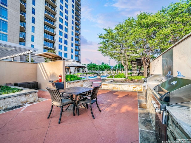 patio terrace at dusk with exterior kitchen, a balcony, and grilling area