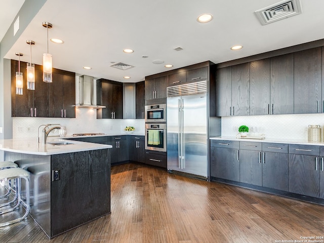 kitchen with hanging light fixtures, dark hardwood / wood-style floors, appliances with stainless steel finishes, wall chimney range hood, and tasteful backsplash