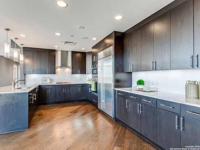 kitchen featuring pendant lighting, hardwood / wood-style floors, backsplash, appliances with stainless steel finishes, and wall chimney range hood