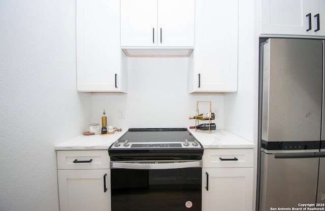 kitchen with stainless steel refrigerator, white cabinetry, and electric range oven