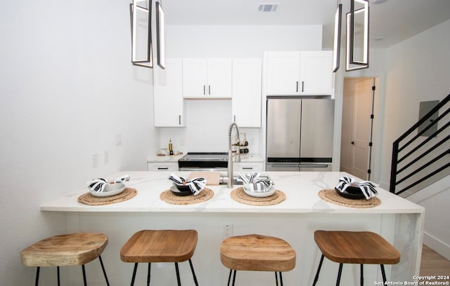 kitchen featuring stainless steel refrigerator, wood-type flooring, white cabinets, and a breakfast bar area