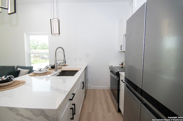 kitchen featuring hanging light fixtures, white cabinets, light hardwood / wood-style flooring, appliances with stainless steel finishes, and sink