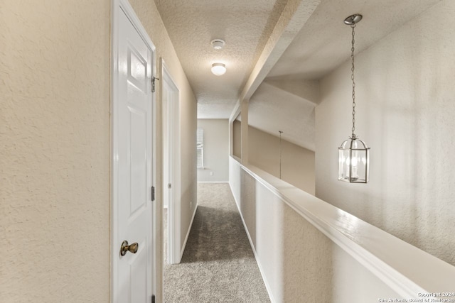 hall with an inviting chandelier, dark carpet, and a textured ceiling