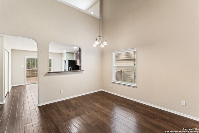 spare room with dark hardwood / wood-style floors, a towering ceiling, and an inviting chandelier