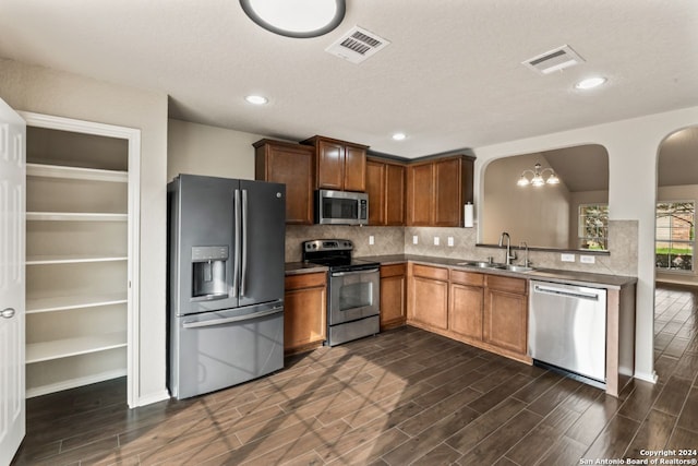 kitchen featuring appliances with stainless steel finishes, sink, backsplash, dark hardwood / wood-style flooring, and an inviting chandelier