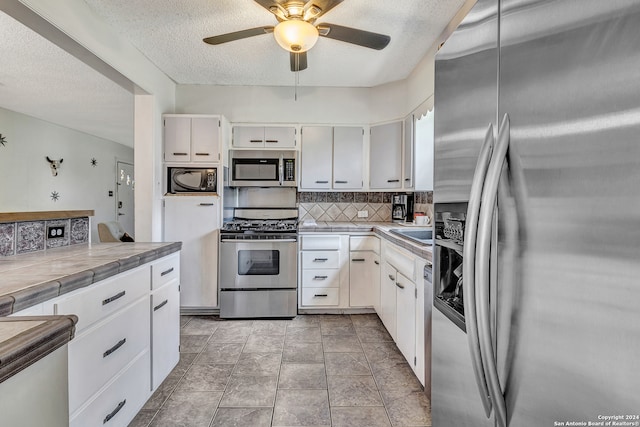 kitchen with appliances with stainless steel finishes, ceiling fan, tasteful backsplash, white cabinetry, and tile countertops