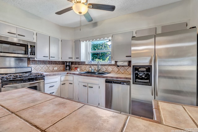 kitchen featuring ceiling fan, sink, tasteful backsplash, stainless steel appliances, and tile counters