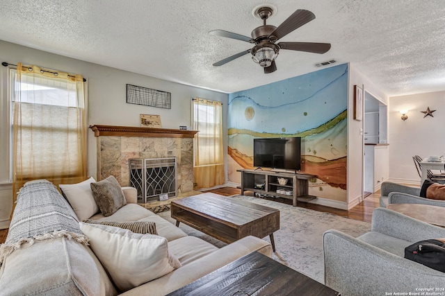 living room featuring wood-type flooring, a tile fireplace, ceiling fan, and a textured ceiling