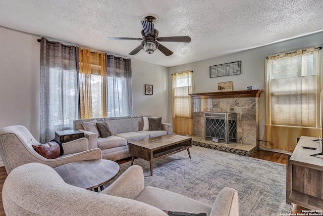 living room with a textured ceiling, ceiling fan, hardwood / wood-style flooring, and a high end fireplace