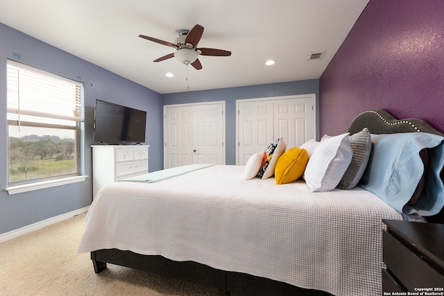 carpeted bedroom with ceiling fan and two closets