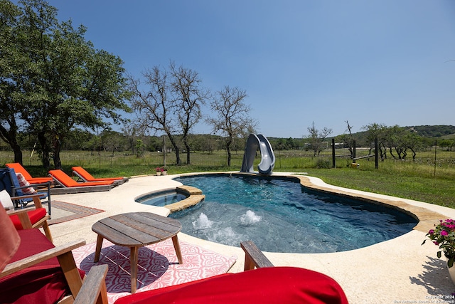 view of pool with a water slide, a lawn, a rural view, and an in ground hot tub