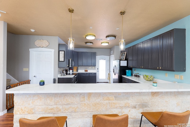 kitchen with pendant lighting, a kitchen breakfast bar, hardwood / wood-style flooring, kitchen peninsula, and stainless steel appliances