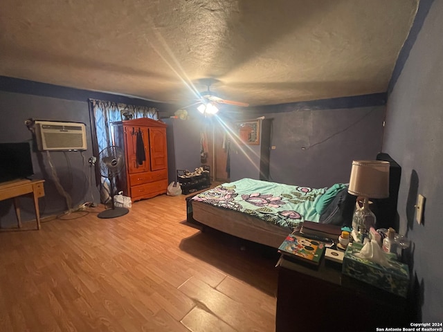 bedroom featuring an AC wall unit, wood-type flooring, ceiling fan, and a textured ceiling