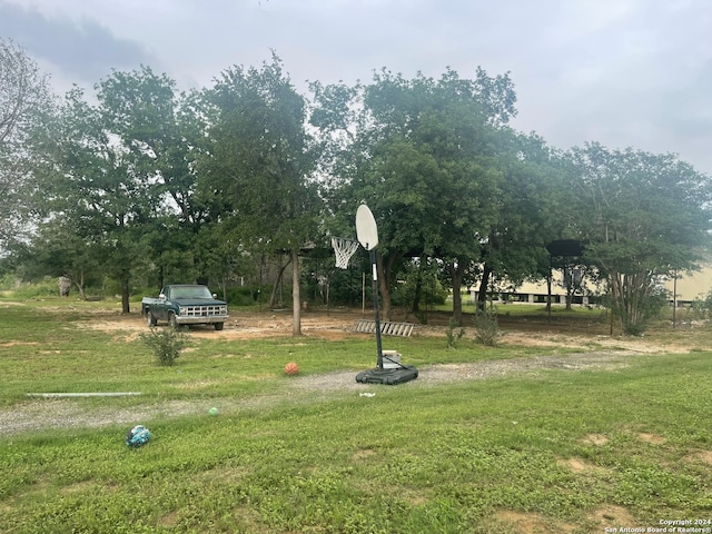 view of home's community featuring basketball hoop and a yard