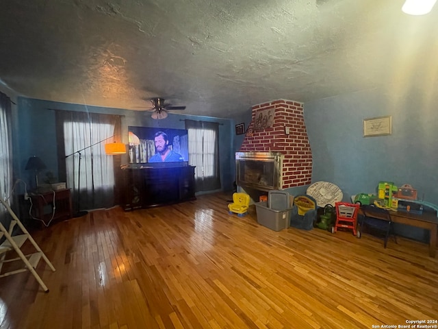 unfurnished living room with a brick fireplace, ceiling fan, brick wall, a textured ceiling, and hardwood / wood-style floors