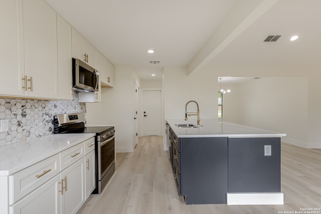 kitchen with light hardwood / wood-style floors, an island with sink, sink, white cabinetry, and appliances with stainless steel finishes