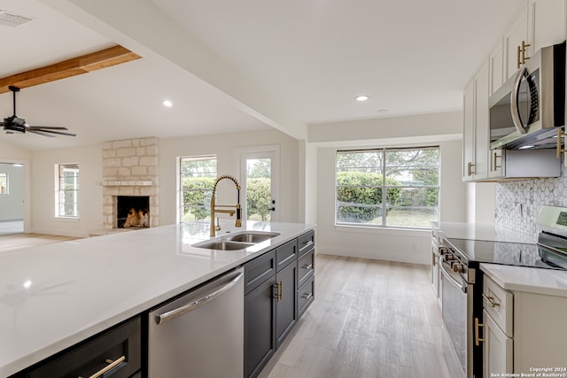 kitchen with beamed ceiling, stainless steel appliances, a fireplace, light wood-type flooring, and sink