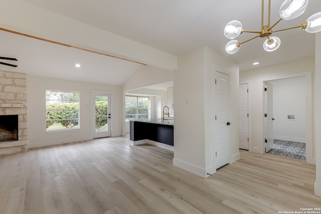 unfurnished living room featuring a stone fireplace, light wood-type flooring, a notable chandelier, sink, and lofted ceiling