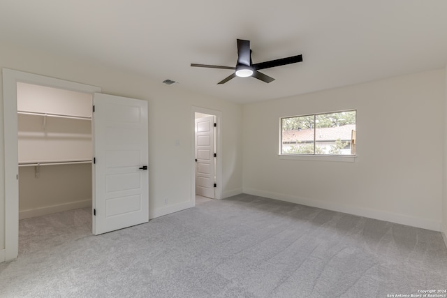 unfurnished bedroom featuring light carpet, a walk in closet, a closet, and ceiling fan