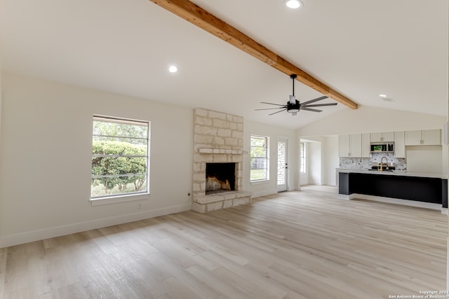 unfurnished living room featuring light hardwood / wood-style floors, ceiling fan, vaulted ceiling with beams, a stone fireplace, and sink