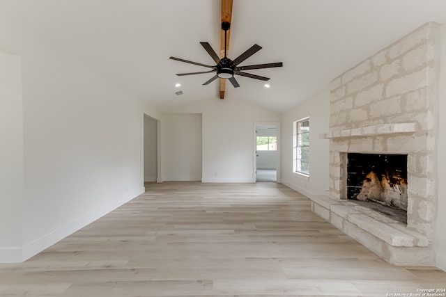 unfurnished living room featuring a stone fireplace, lofted ceiling with beams, ceiling fan, and light hardwood / wood-style flooring