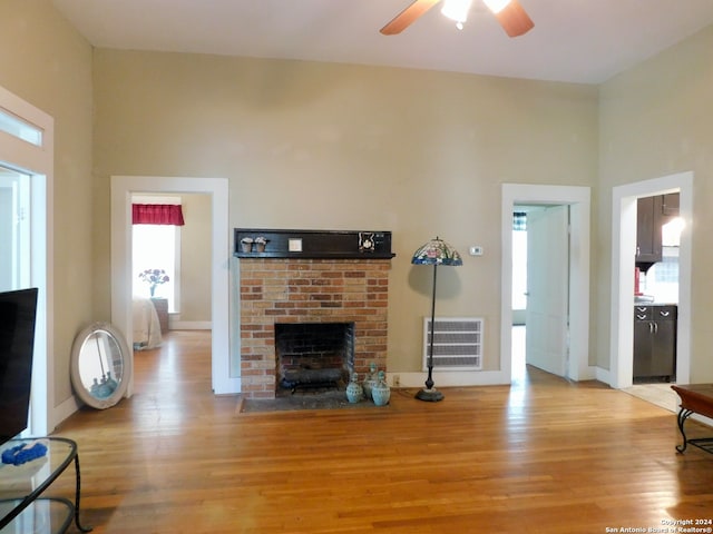 living room with a towering ceiling, ceiling fan, light hardwood / wood-style floors, and a fireplace