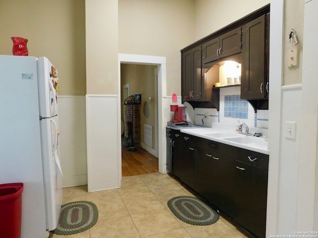 kitchen with white fridge, light hardwood / wood-style flooring, backsplash, dark brown cabinets, and sink