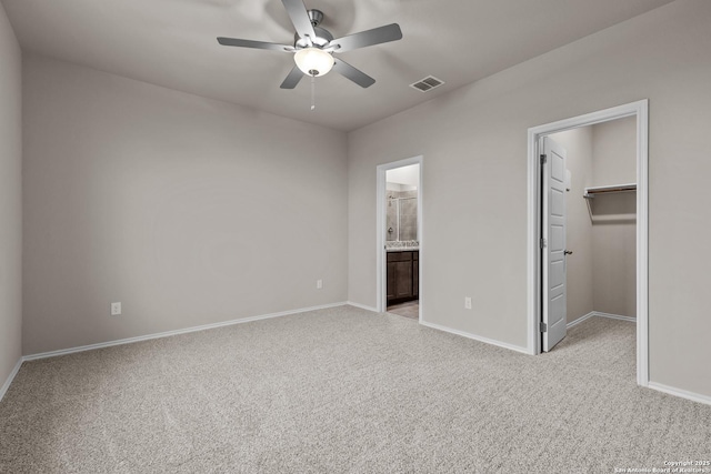 unfurnished bedroom featuring a spacious closet, ceiling fan, ensuite bathroom, light colored carpet, and a closet