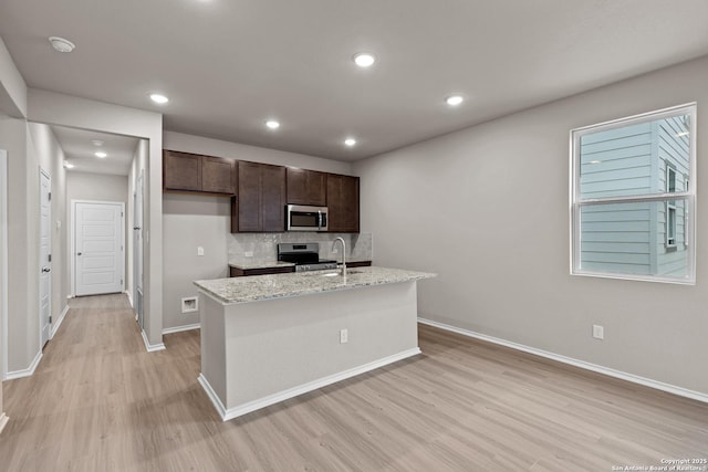 kitchen with decorative backsplash, an island with sink, light stone counters, and appliances with stainless steel finishes