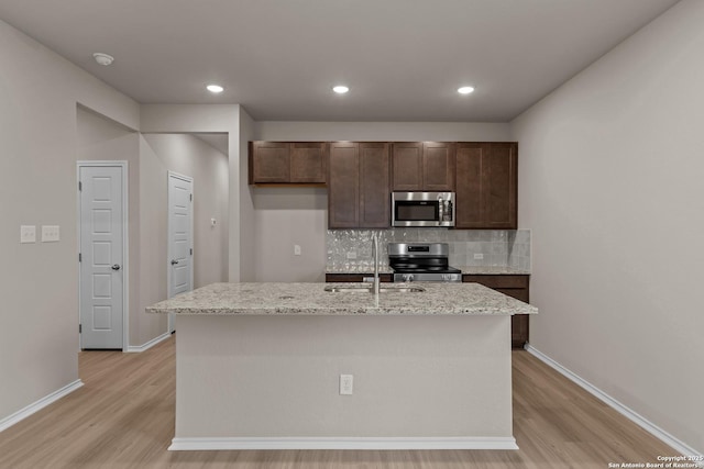 kitchen with decorative backsplash, appliances with stainless steel finishes, light stone countertops, and a kitchen island with sink