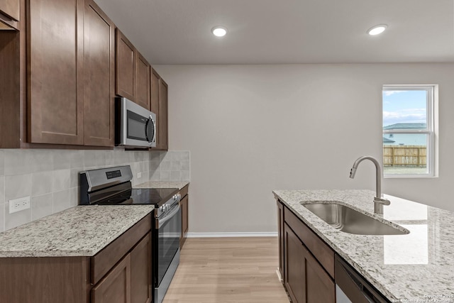 kitchen featuring sink, light hardwood / wood-style flooring, light stone countertops, tasteful backsplash, and stainless steel appliances