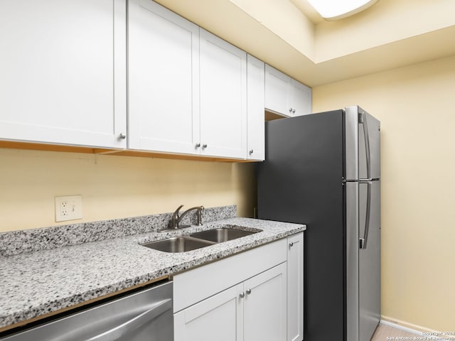 kitchen with appliances with stainless steel finishes, white cabinetry, sink, and light stone countertops