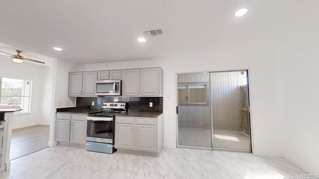 kitchen with appliances with stainless steel finishes, gray cabinets, tasteful backsplash, light tile flooring, and ceiling fan