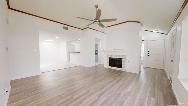 unfurnished living room with crown molding, ceiling fan, a tiled fireplace, and hardwood / wood-style floors